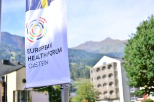 The flag of European Health Forum Gastein before the scenery of Bad Hofgastein and the majestic Gastein valley mountains.