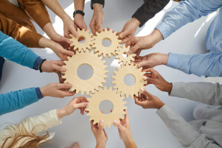 Business people or office workers hold wooden gears that symbolize well-coordinated teamwork. Top view close up of hands of multiracial men and women standing in circle. Concept business cooperation